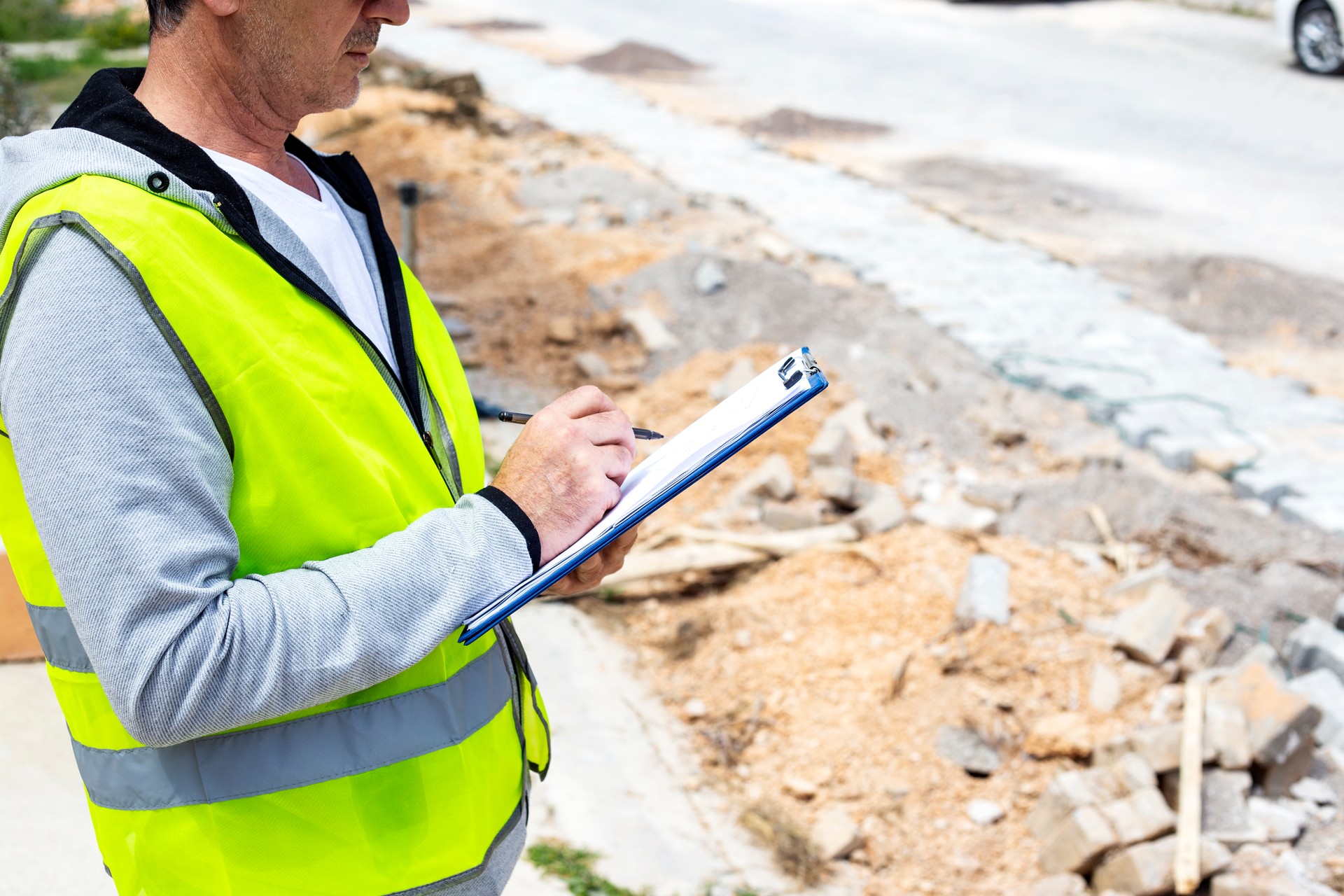 Architect engineer in a white helmet and reflective vest is writing on clipboard at construction site in front of a building